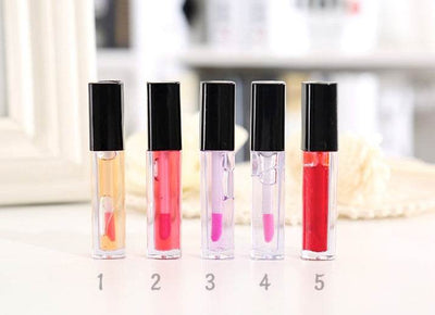 Set of five liquid lipsticks and lip glosses in various shades with black caps on a white surface