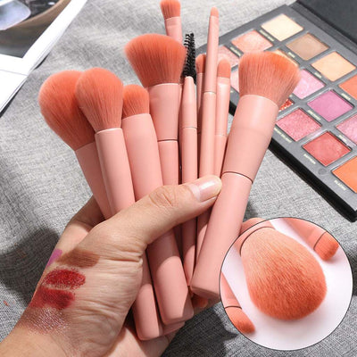 Set of pink cosmetic brush make up tools with wooden handles and soft nylon bristles held in hand above eyeshadow palette