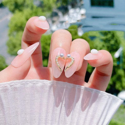 Close-up of manicured nails with pink polish and DIY heart-shaped alloy and rhinestone nail art decoration.
